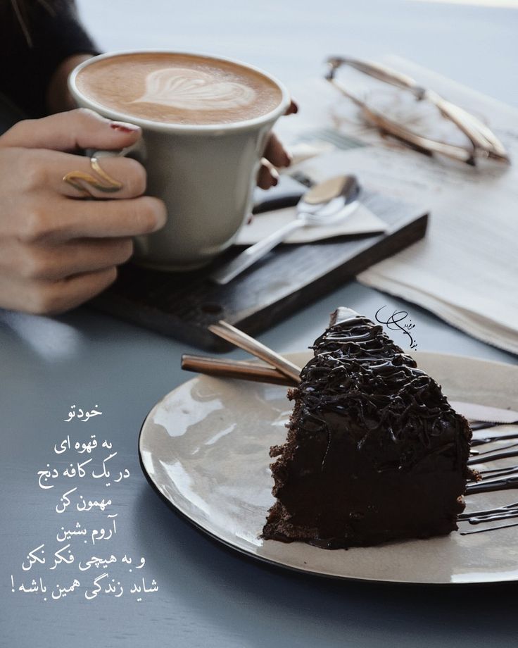 a piece of chocolate cake on a plate with a cup of coffee in the background