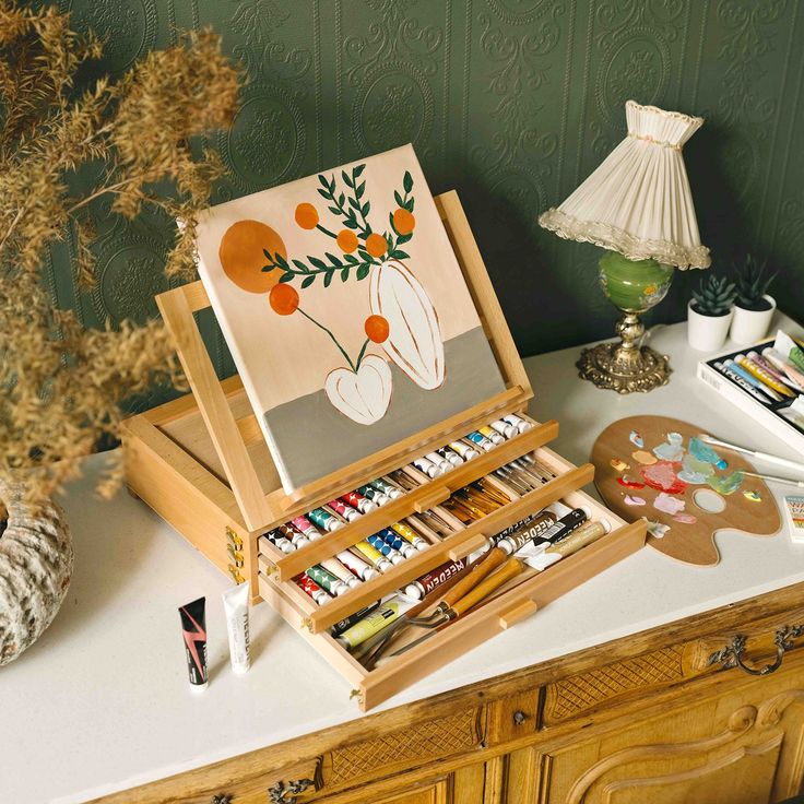 a wooden easel with art supplies on top of a table next to a lamp