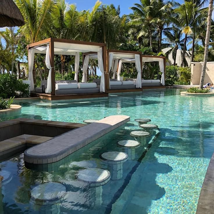 an outdoor swimming pool with lounge chairs and umbrellas on the side, surrounded by palm trees