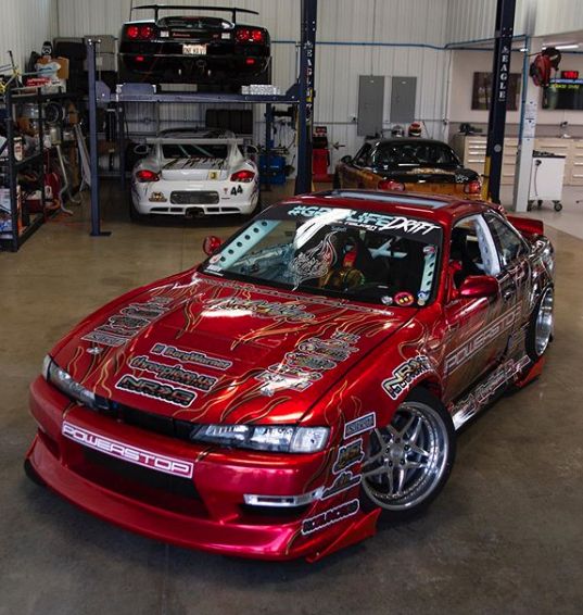 a red car parked inside of a garage next to other cars and tools on shelves