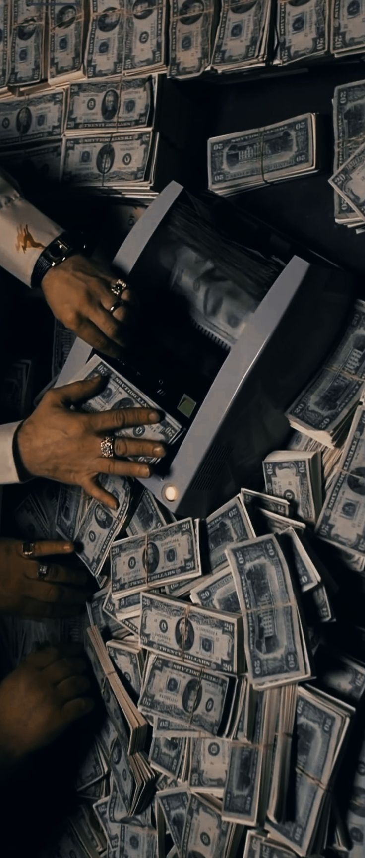 two hands reaching into a cash register surrounded by stacks of dollar bills on top of each other