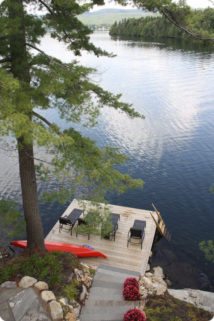 a dock with chairs on it next to the water and trees in the foreground