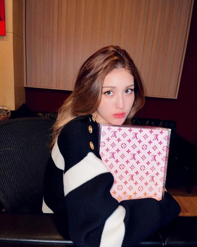 a woman sitting on a couch holding a pink and white box with louis vuitton