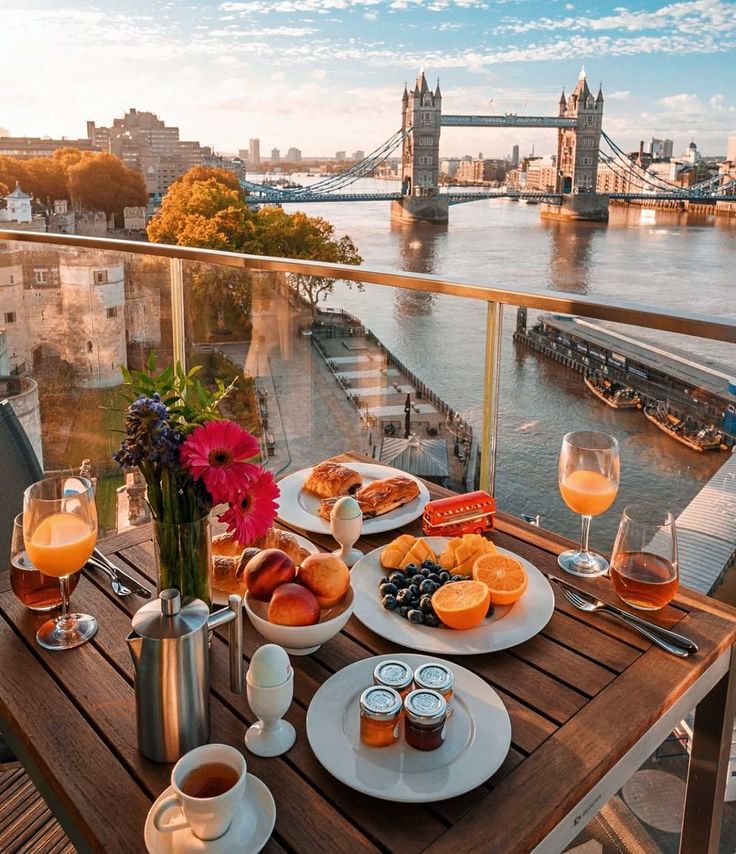 an outdoor table with food and drinks on it, overlooking the river thames in london