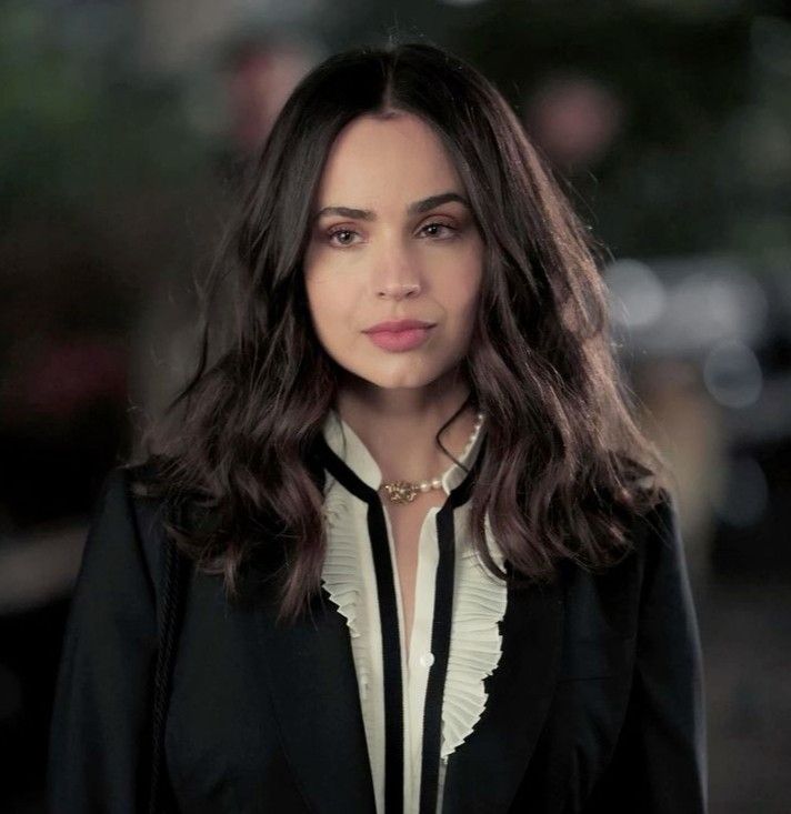 a woman with long dark hair wearing a black suit and white shirt is looking at the camera