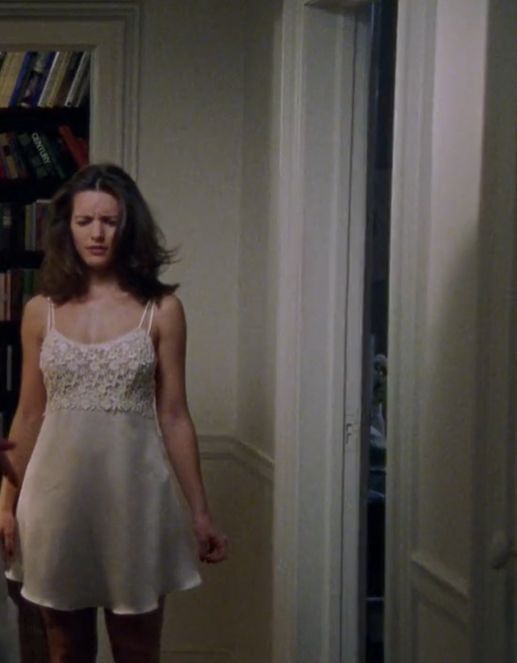 a woman in a white dress is standing by a bookshelf