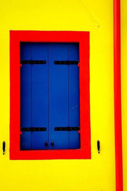 a red and blue window on the side of a yellow wall