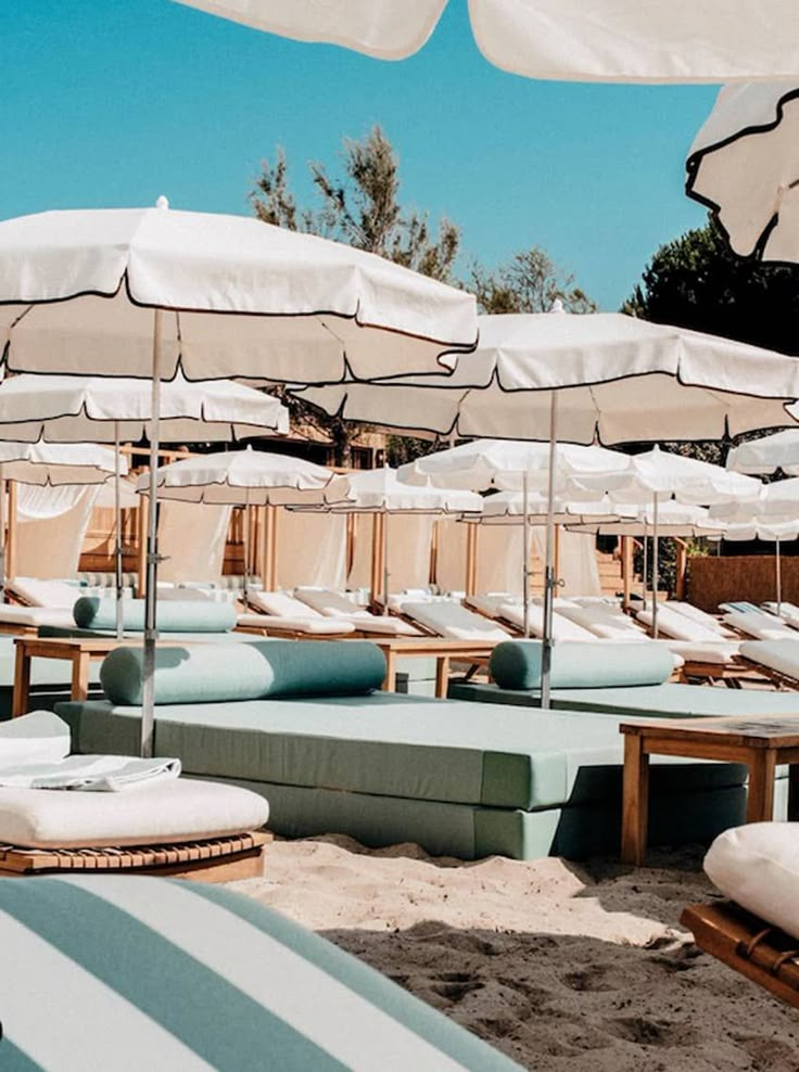 lounge chairs and umbrellas are lined up on the sand at an outdoor beach resort