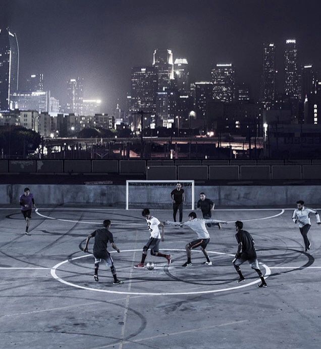 a group of young men playing soccer on top of a cement field in front of a city skyline