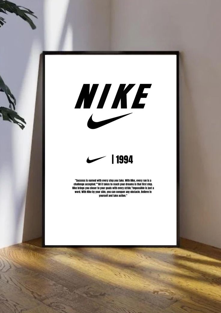 a black and white nike poster sitting on top of a wooden floor next to a plant