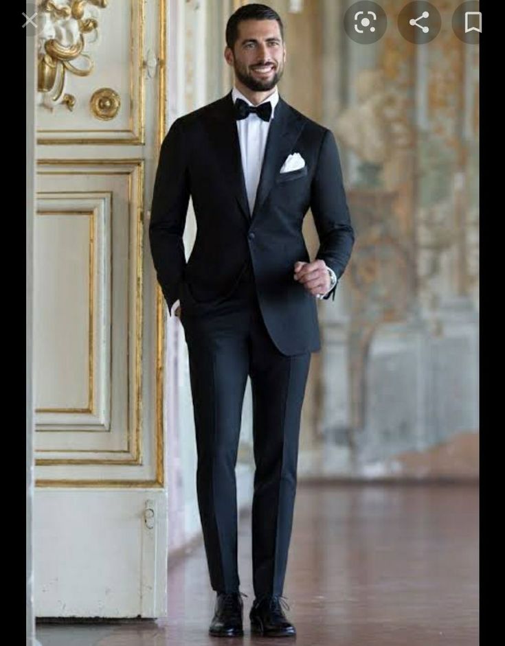 a man in a tuxedo standing next to an open door with his hands on his hips