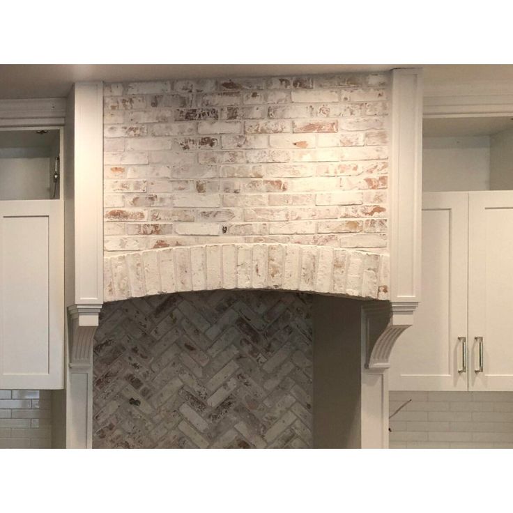 a kitchen with white cabinets and a brick fireplace in the center, surrounded by cupboards