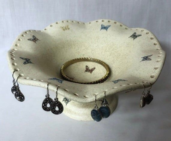 a white bowl with earrings hanging from it's sides and a ring holder in the middle