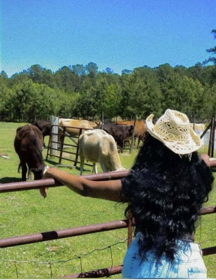 a woman wearing a straw hat looking at cows behind a fence