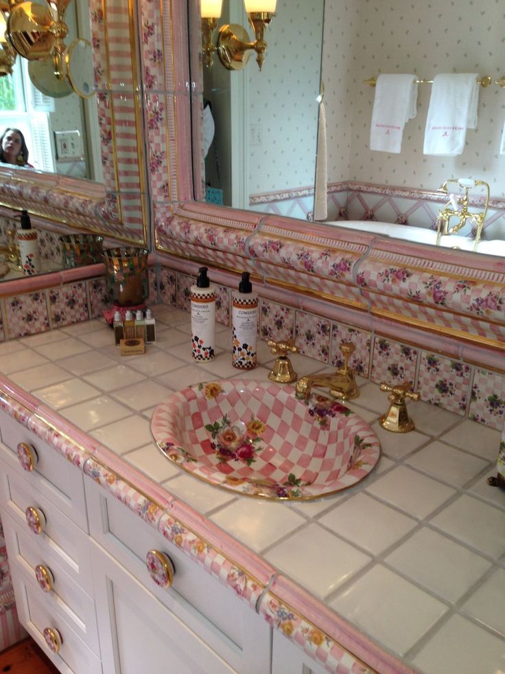 a bathroom sink with pink and white tiles on the counter top next to a mirror