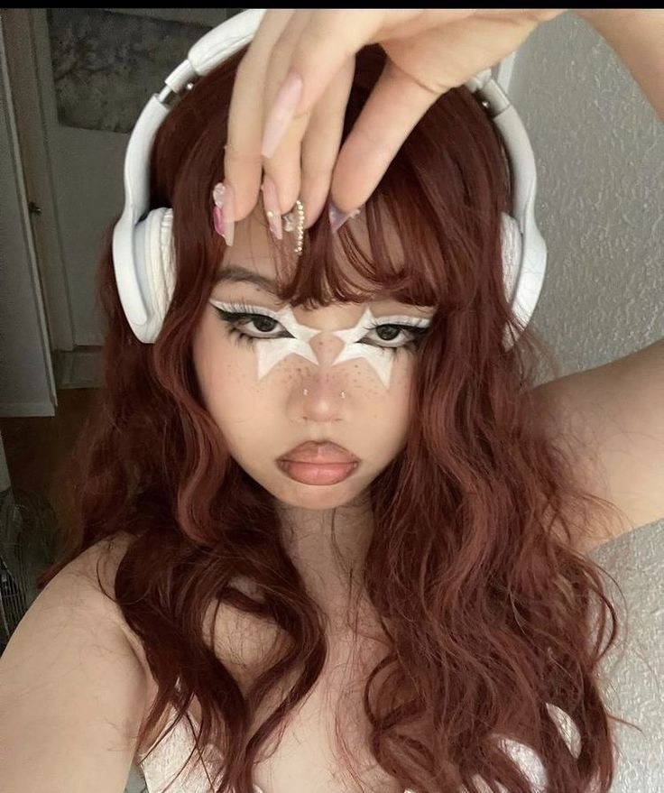 a woman with headphones on her ears is wearing white makeup and has long red hair