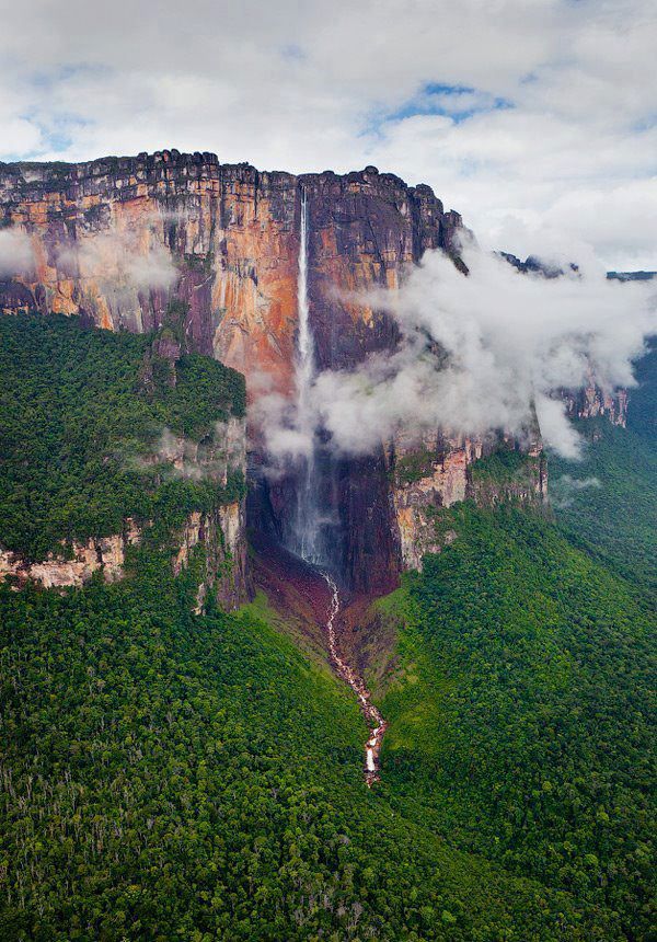 an aerial view of a waterfall surrounded by lush green trees and mountains in the distance