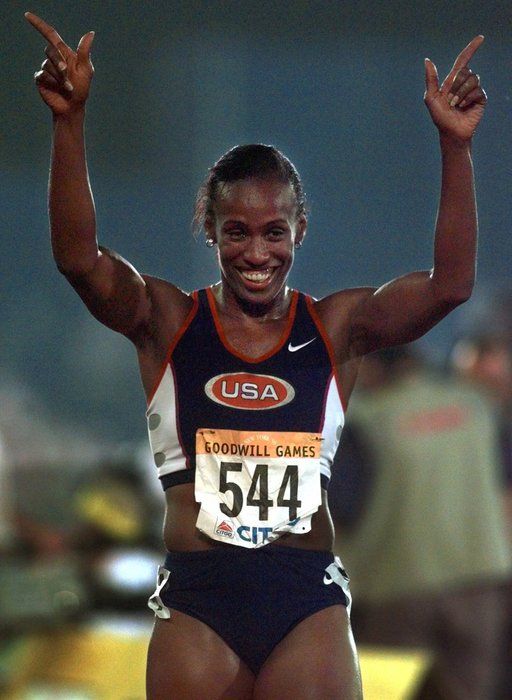 a woman is smiling and holding her hands up in the air as she crosses the finish line