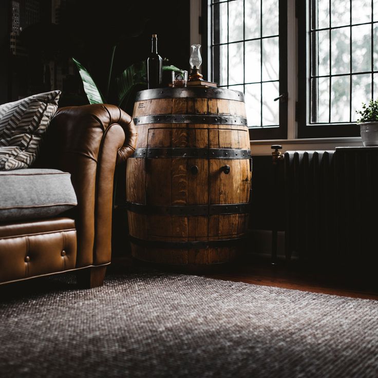 a living room filled with furniture and a wooden barrel next to a window on top of a rug