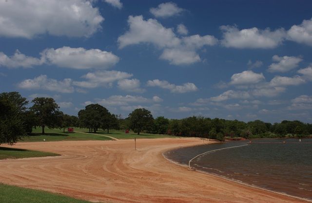 a dirt road next to the water with trees on both sides and clouds in the sky