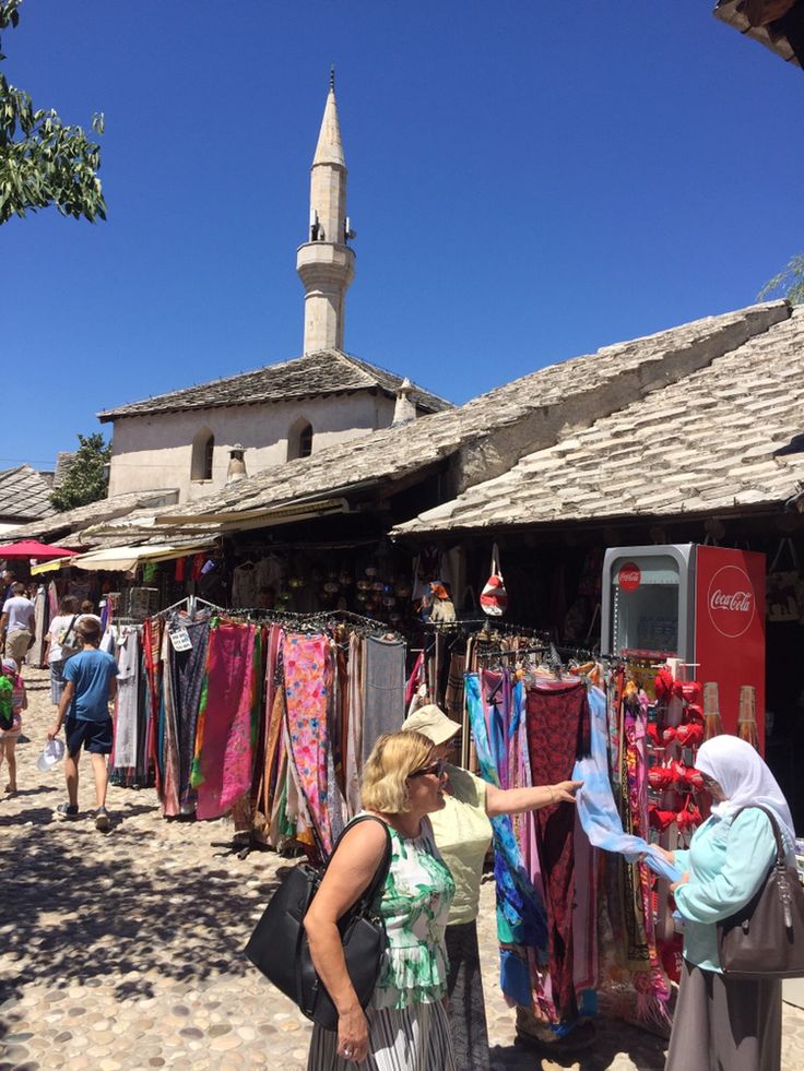 two women standing in front of a market with clothes hanging on the rack and an old church in the background