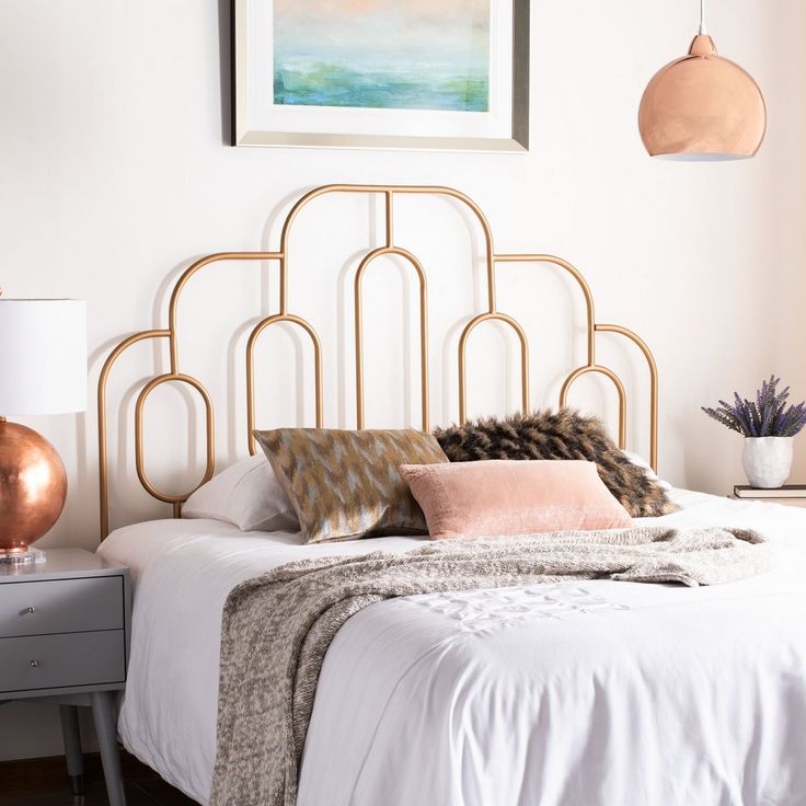 a white bed with gold headboard and pink pillows in a small room next to a painting on the wall