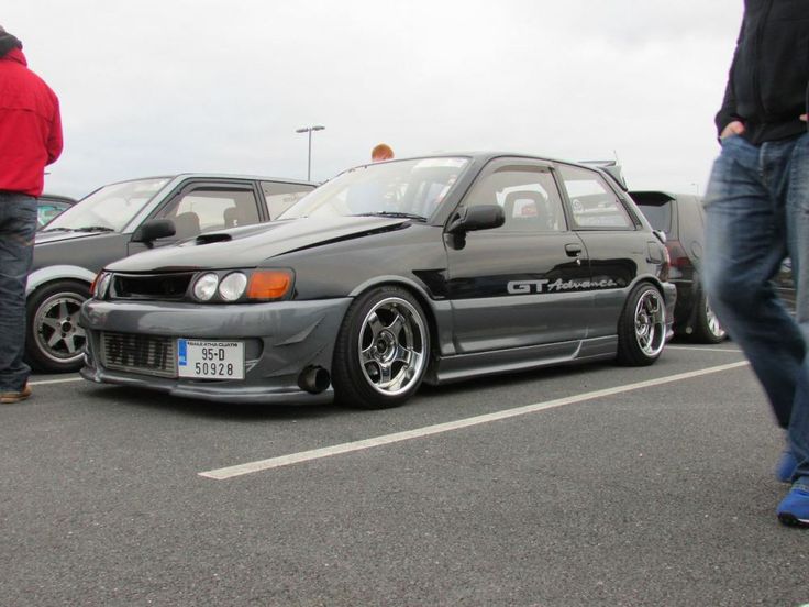 a gray car parked in a parking lot next to other cars and people standing around