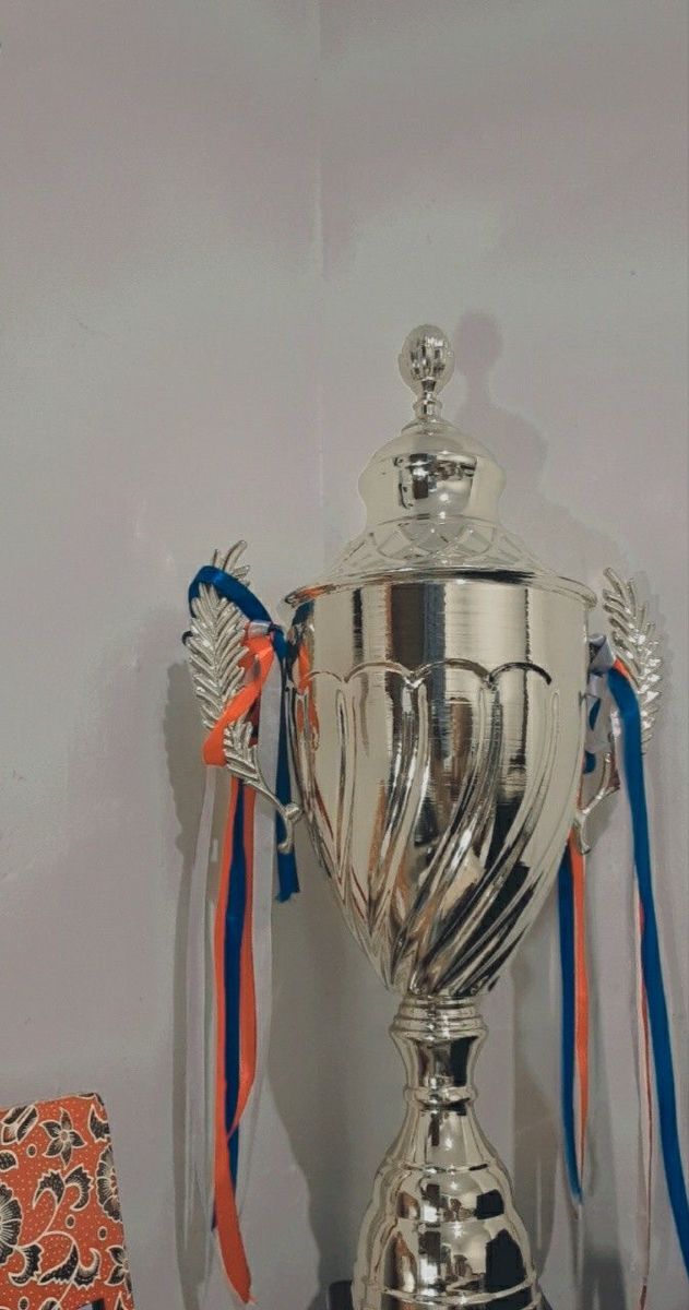 a silver trophy sitting on top of a table next to an orange and blue ribbon