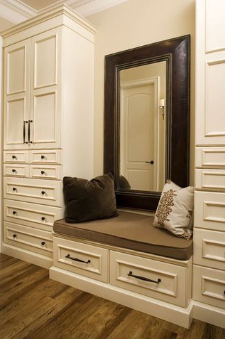 a large mirror sitting on top of a wooden bench next to white cabinets and drawers