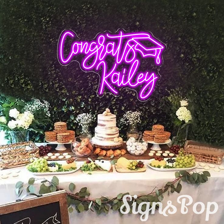 a table topped with cakes and desserts under a neon sign