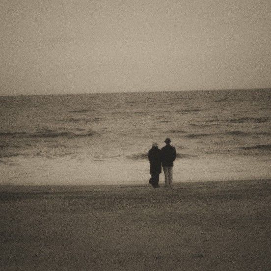 two people standing on the beach looking out at the ocean