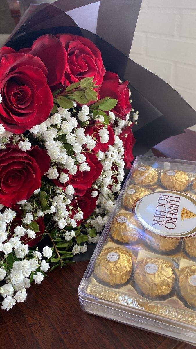 a bouquet of red roses and white flowers next to a box of chocolates on a table