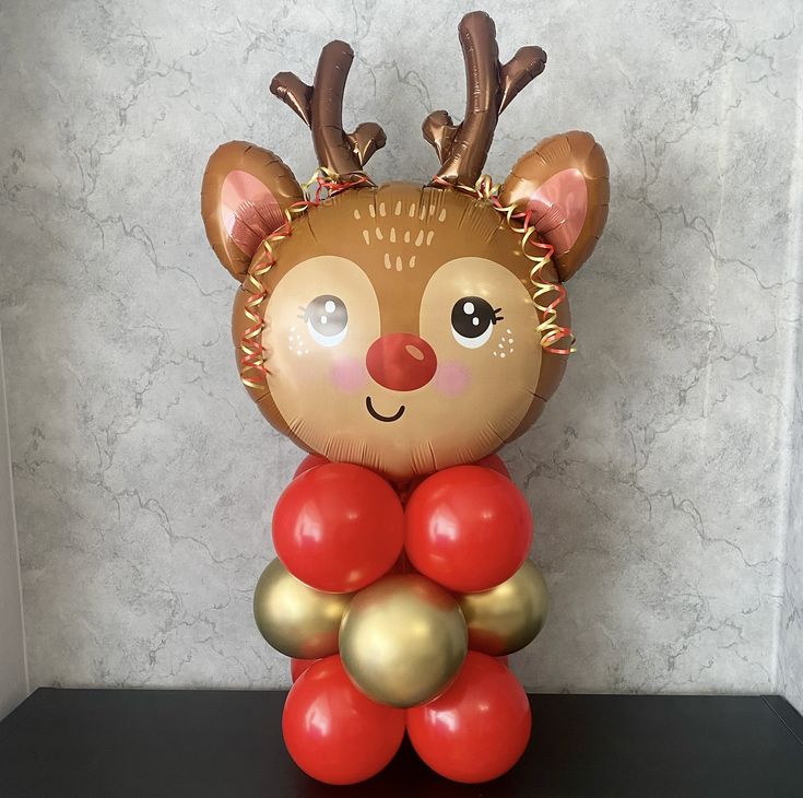 a reindeer balloon sitting on top of a black shelf with red and gold balloons in it's mouth