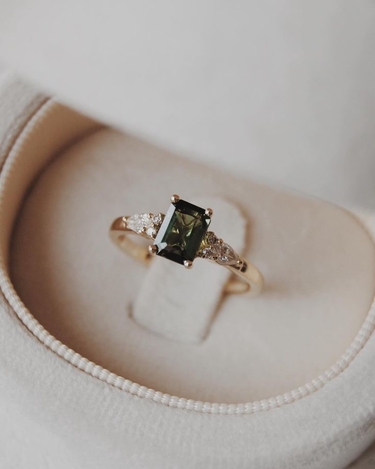 an engagement ring with a green tourmaline surrounded by white diamonds in a box