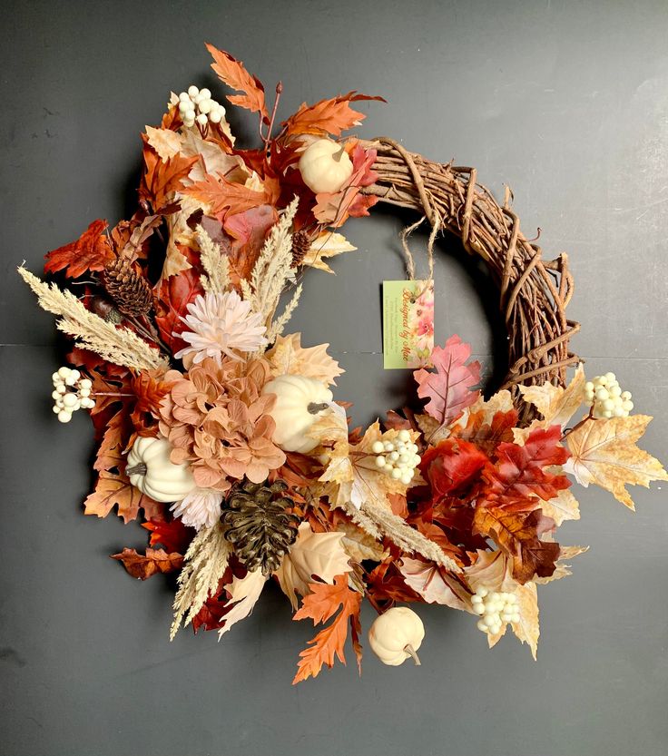 a wreath with autumn leaves and pumpkins hanging on a wall