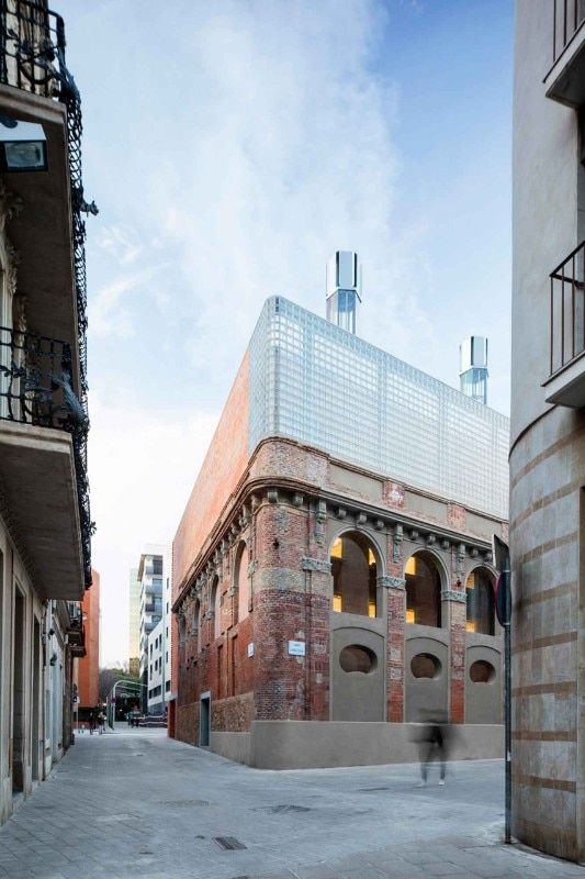 a person walking down the street in front of an old brick building with a glass roof