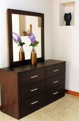 two vases with flowers sit on top of a dresser in front of a mirror