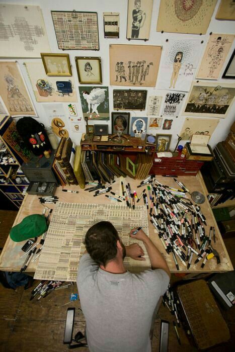 a man sitting at a table working on a project in front of many framed pictures