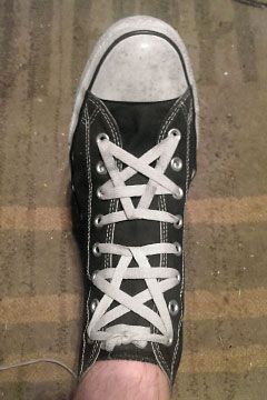 a person's feet with black and white converse shoes tied up to the side