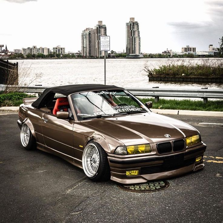 a brown car parked in front of a body of water with tall buildings in the background