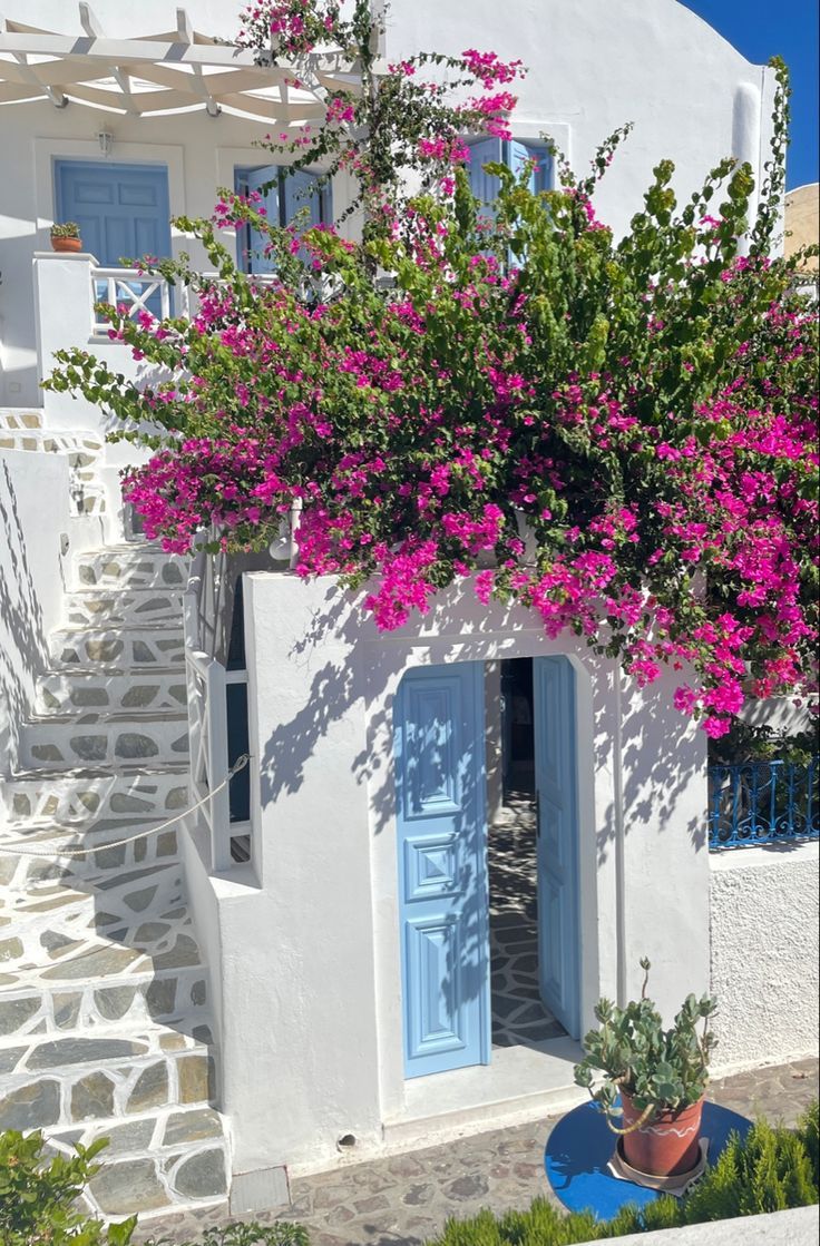 a white house with blue doors and pink flowers