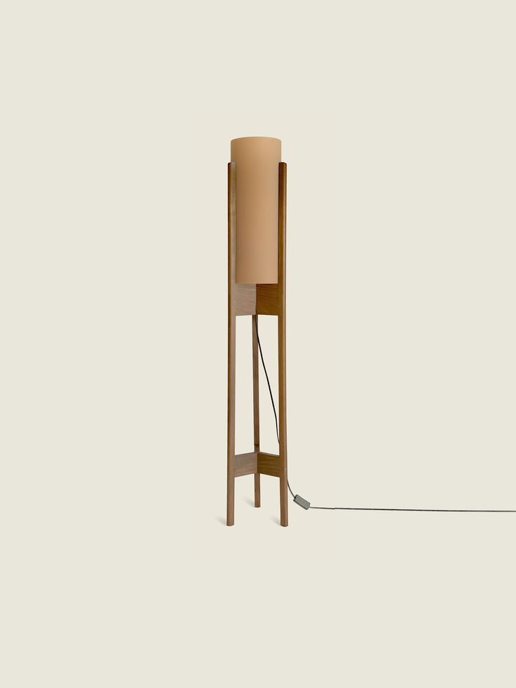 a wooden floor lamp with a beige shade on it's side and a cord attached to the base