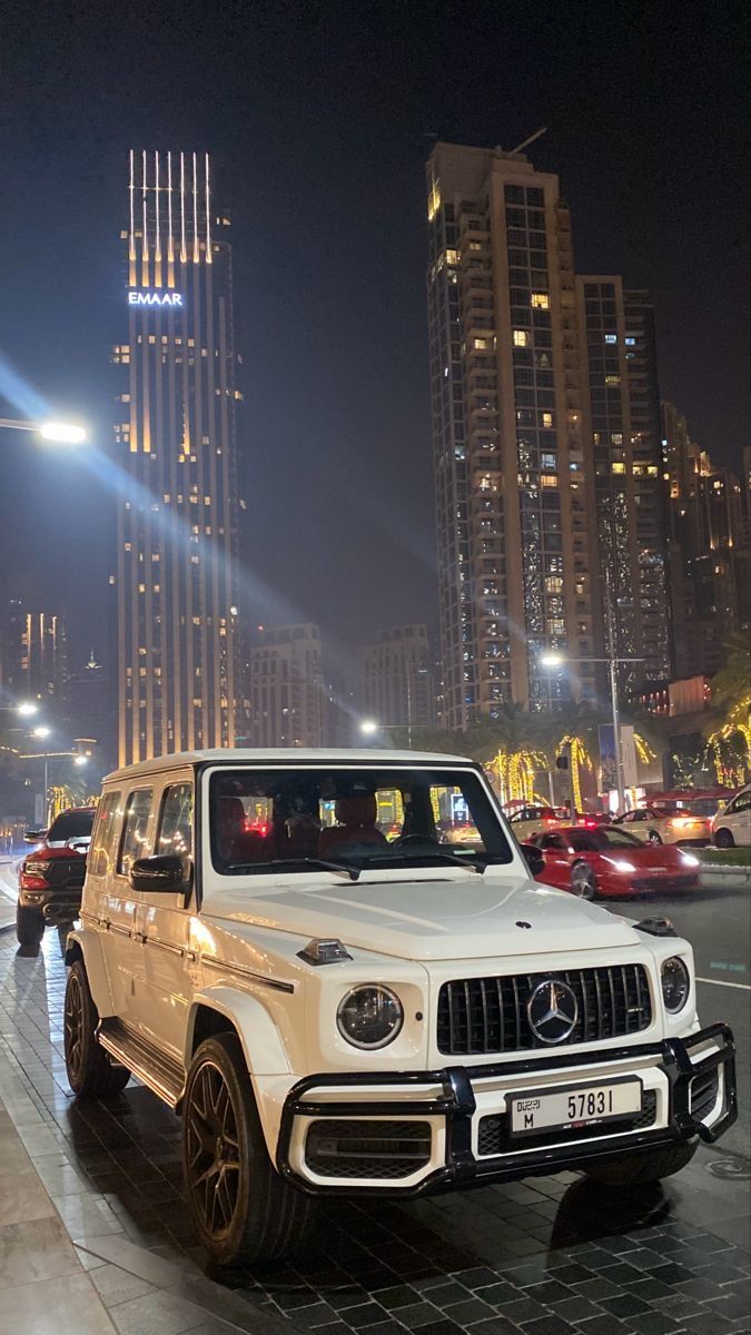 a white mercedes g - class parked in front of tall buildings