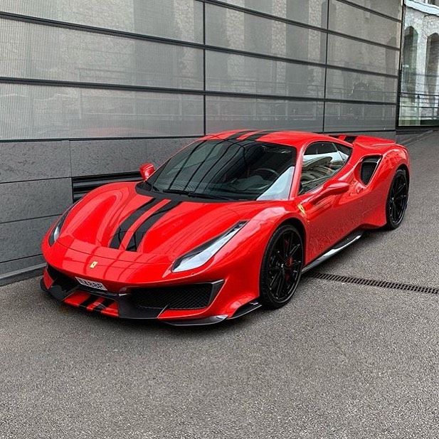 a red sports car is parked in front of a gray wall with black stripes on it