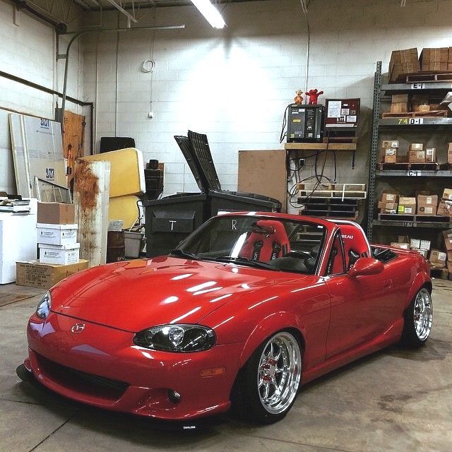 a red sports car parked in a garage next to shelves and other items on the floor