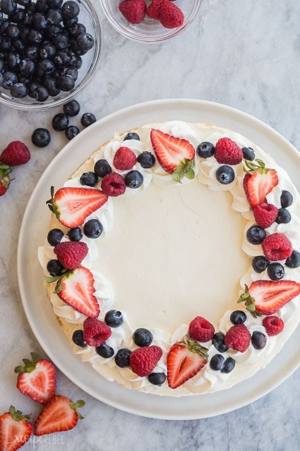 a cake decorated with berries and blueberries on a white plate next to bowls of strawberries