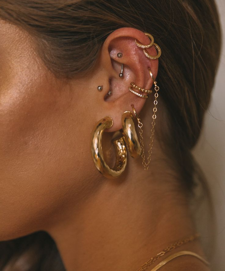 a close up of a person with ear piercings and gold chains on their ears