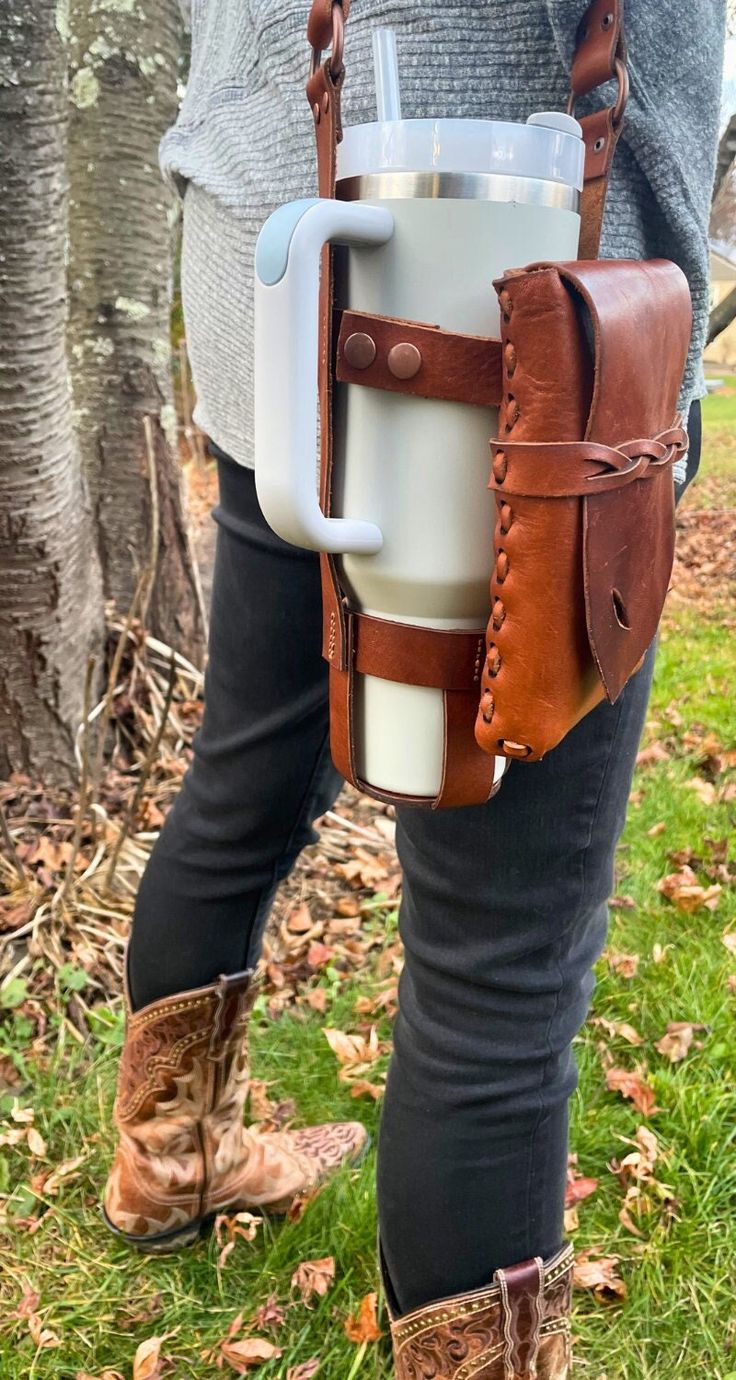 "Try our premium handstitched leather water bottle holder made specifically to carry around your Stanley cup. *Bottle/tumbler is NOT included in your purchase. **The pouch IS removable. This bottle carrier is made with 100% genuine cowhide leather. PLEASE NOTE: Due to the organic nature of leather, your product may not look exactly identical to the listing photo(s).  ✦COLORS: Medium Brown, Black ✦STRAP SIZE: One size (strap is adjustable from 39\" to 42\" measured from ring to ring) ✦POUCH SIZE: Leather Kitchen Accessories, Leather Water Bottle Holder, Leather Projects Ideas, Leather Bottle Holder, Leather Water Bottle, Cup Carrier, Diy Leather Projects, Water Bottle Carrier, Hiker Gifts