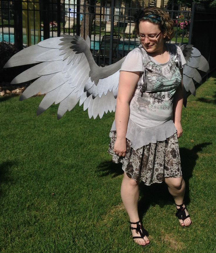 a woman is standing in the grass with her wings spread out and there is a large bird behind her