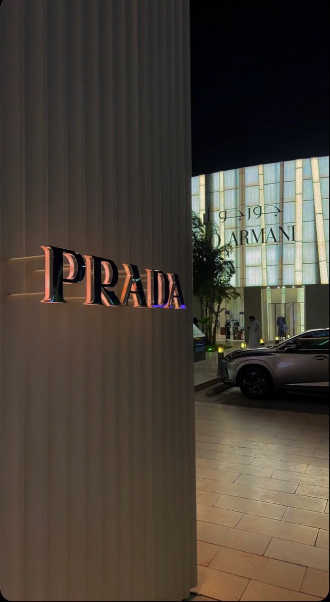 the word prada is lit up at night in front of a building with cars parked outside